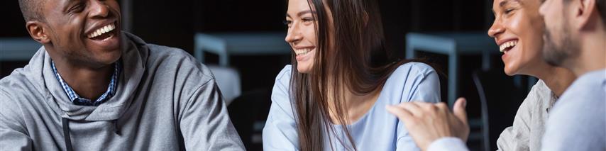 Group of four people laughing while sat around a table drinking coffee.